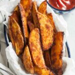 Roasted potato wedges on a piece of parchment paper in a bowl.