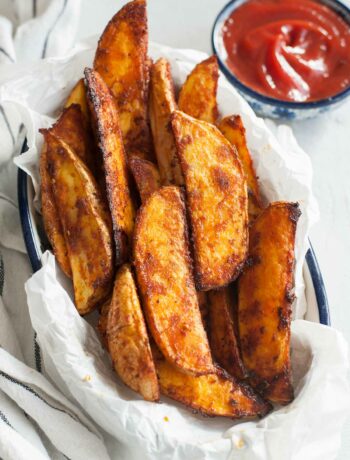 Roasted potato wedges on a piece of parchment paper in a bowl.