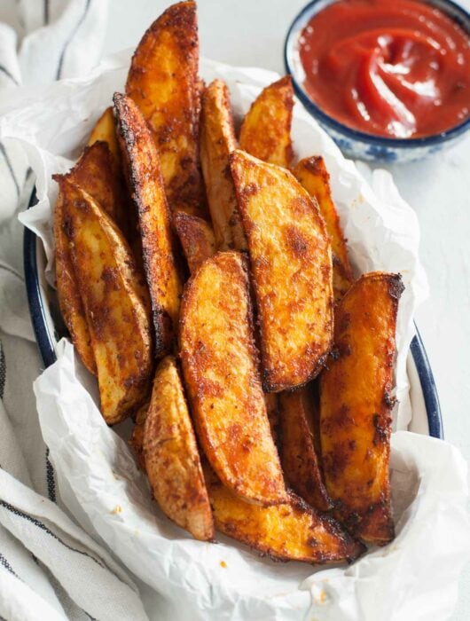 Roasted potato wedges on a piece of parchment paper in a bowl.