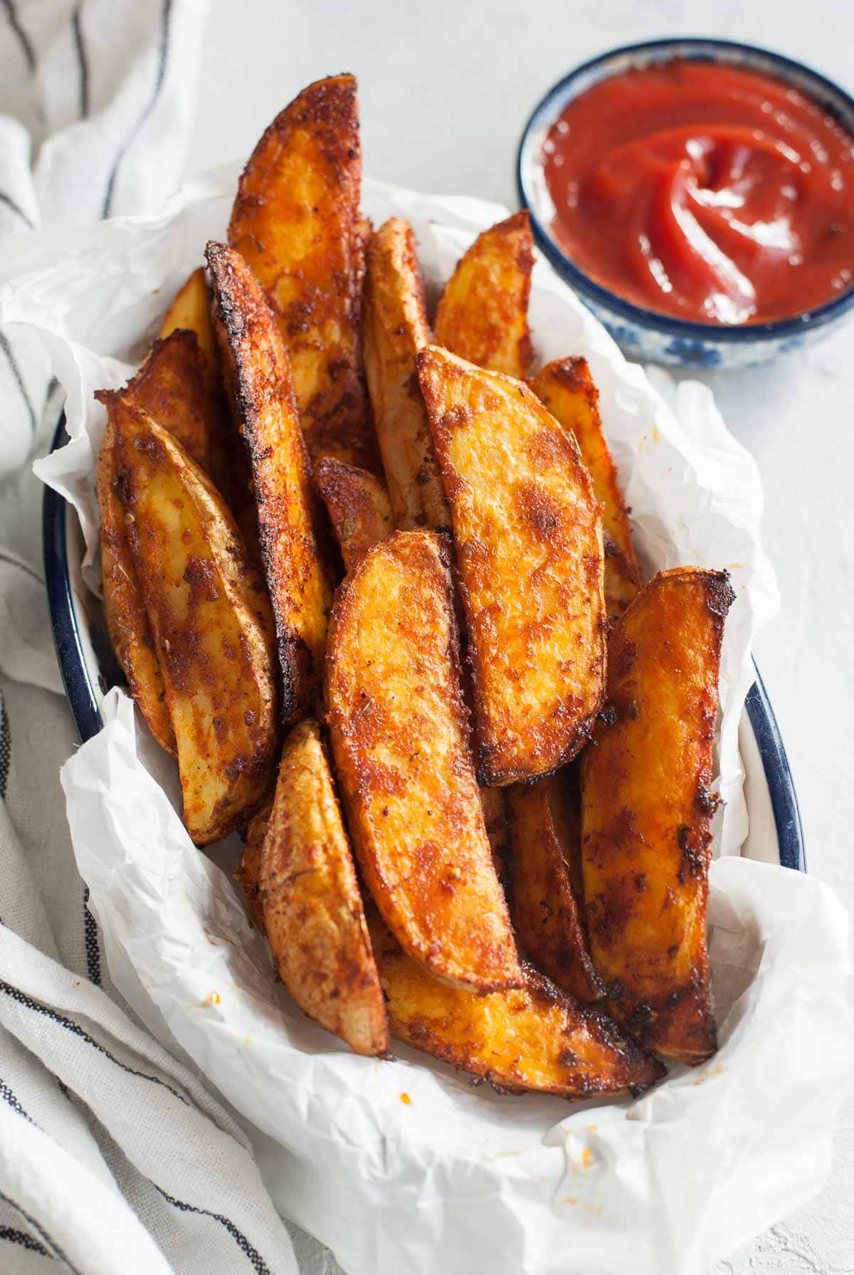 Roasted potato wedges on a piece of parchment paper in bowl on towel.