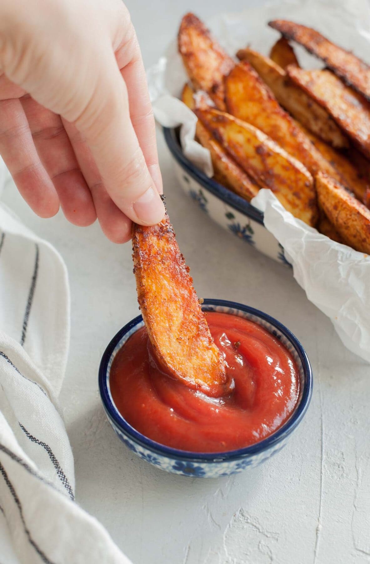Spicy roasted potato wedges are being dipped in ketchup.