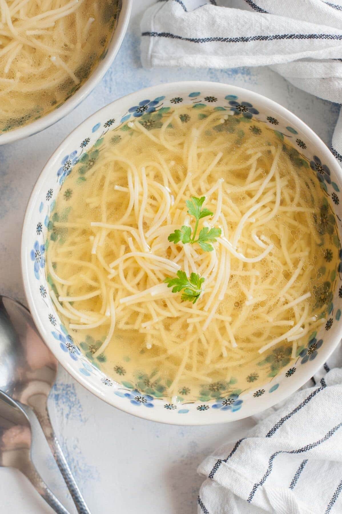 Rosół soup in a white blue bowl served with pasta and topped with parsley.