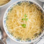 Rosół soup in a white blue bowl served with pasta and topped with parsley.