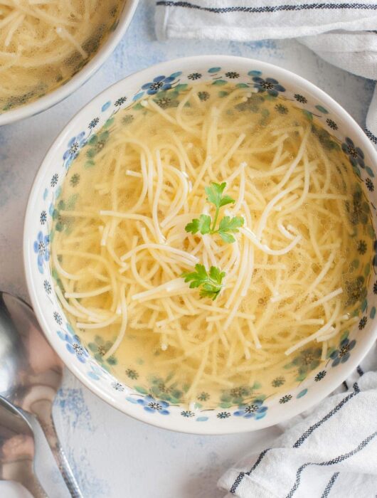 Rosół soup in a white blue bowl served with pasta and topped with parsley.