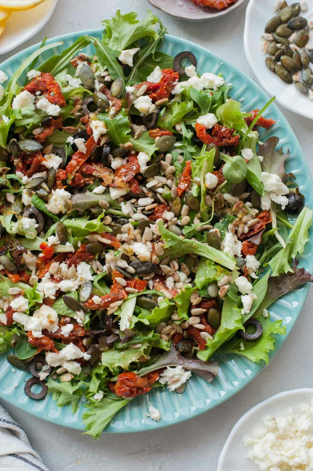 Sun-dried tomatoes salad with olives and feta on a green plate.