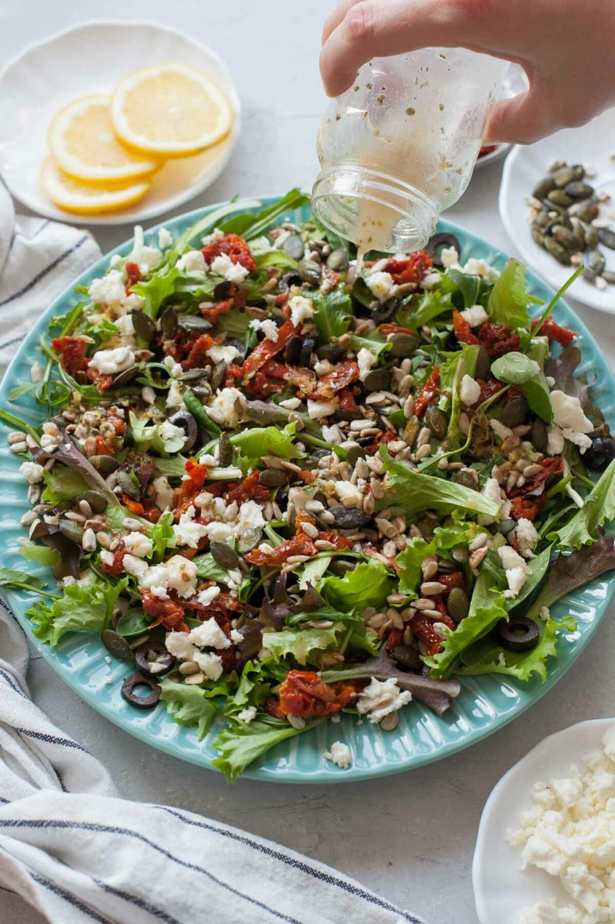 Lemon oregano dressing is being poured over a sun-dried tomato salad.