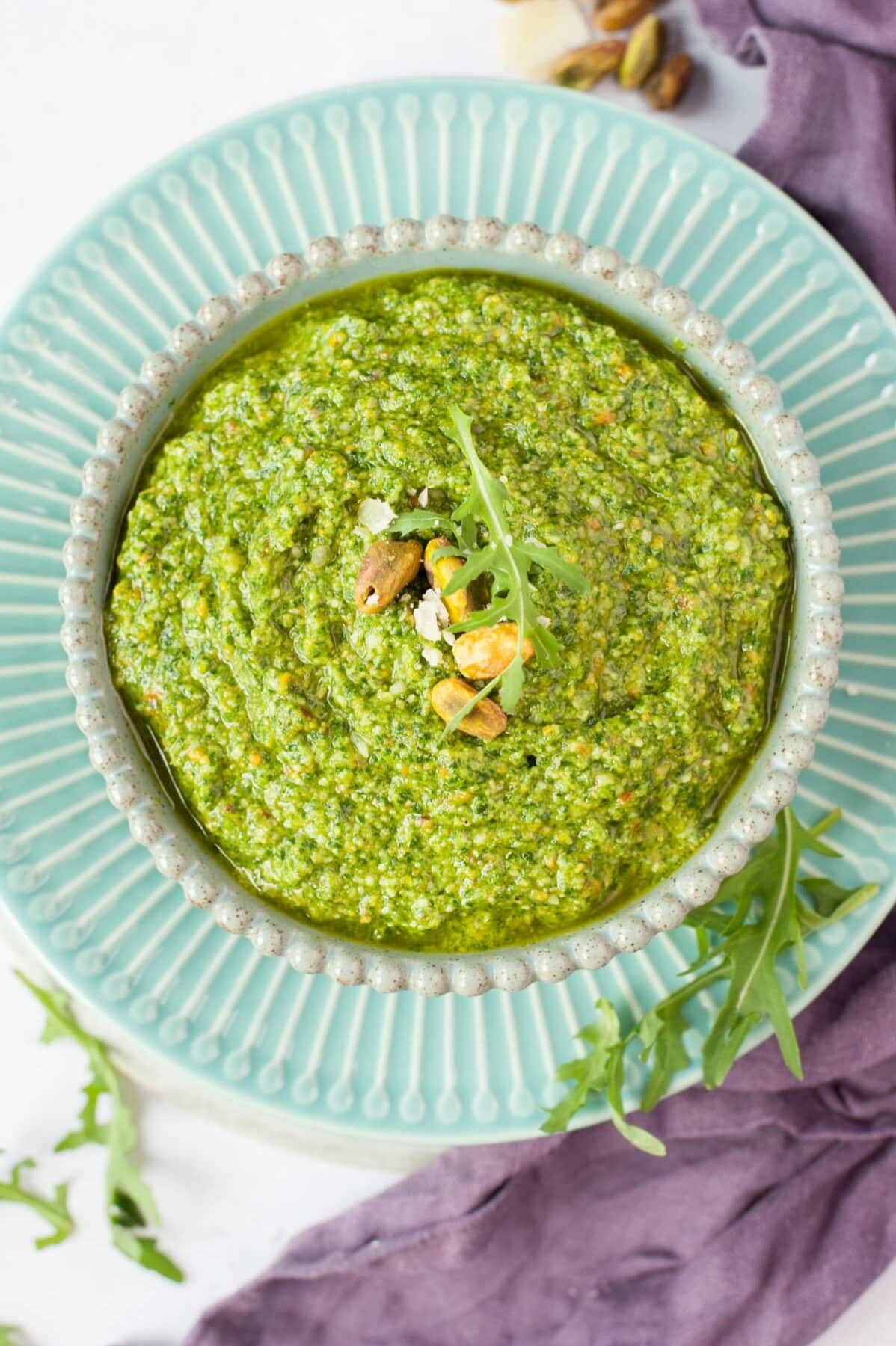 Arugula pistachio pesto in a green bowl topped with arugula leaves and pistachios.