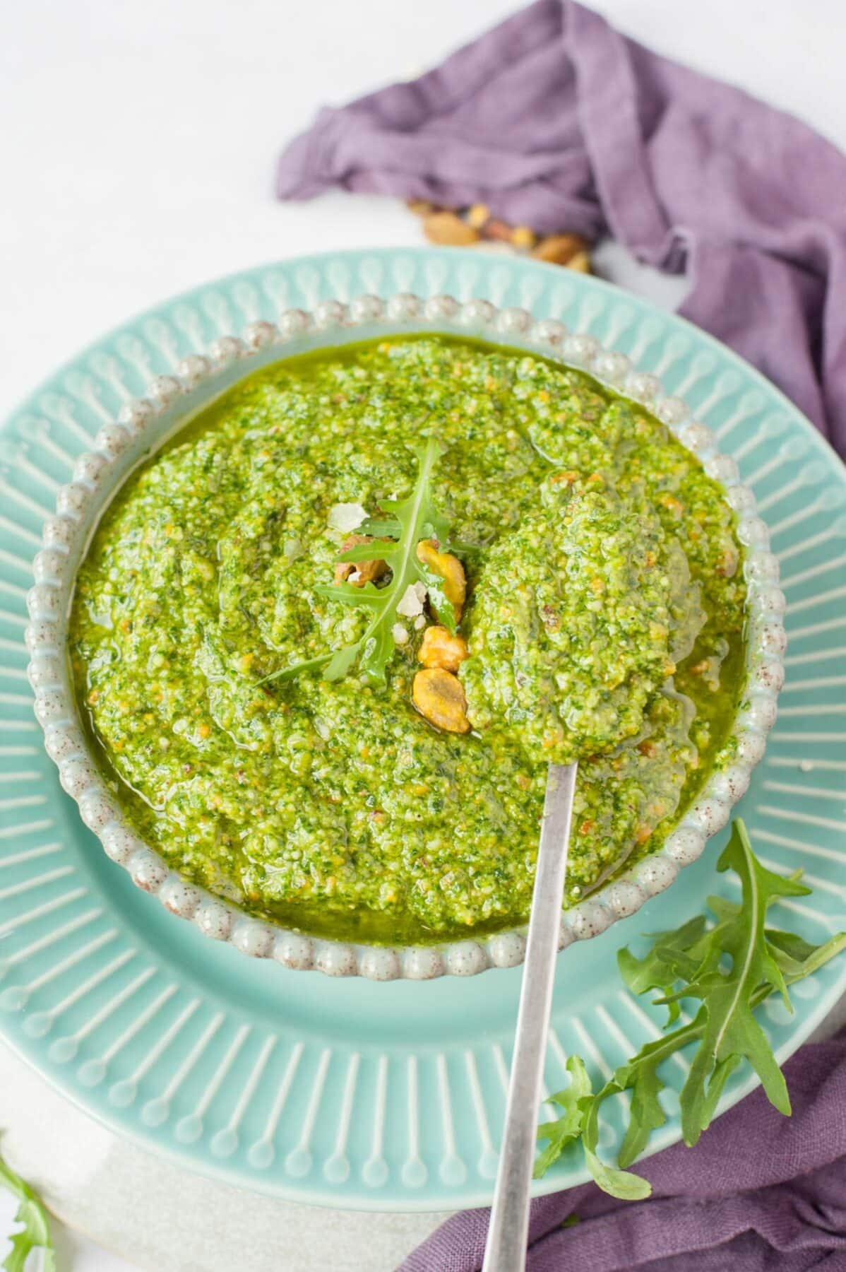 Arugula pistachio pesto in a green bowl, topped with parmesan, arugula leaves and pistachios.