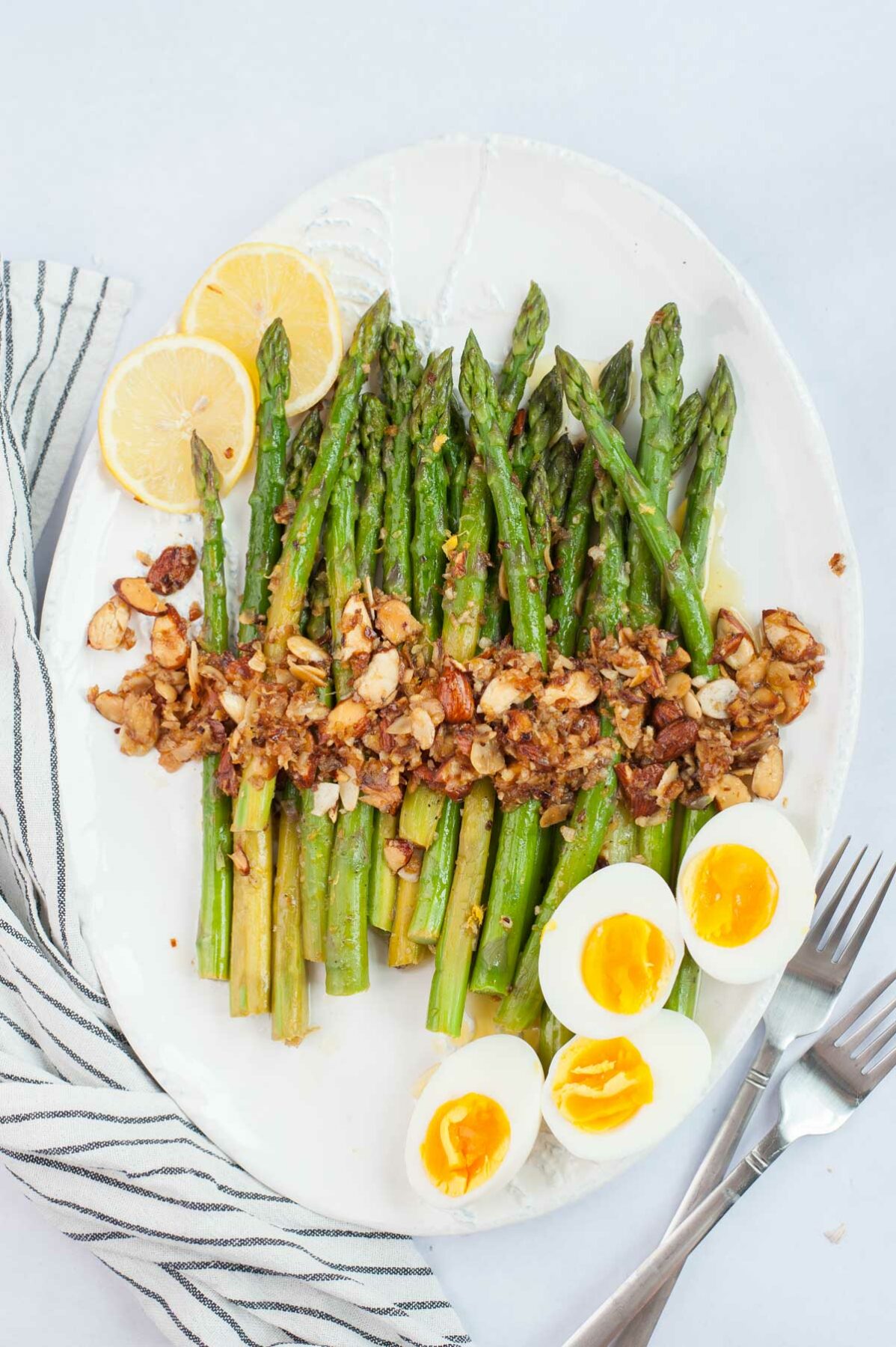 Asparagus almondine on a white plate with lemon slices and halved eggs on the side.