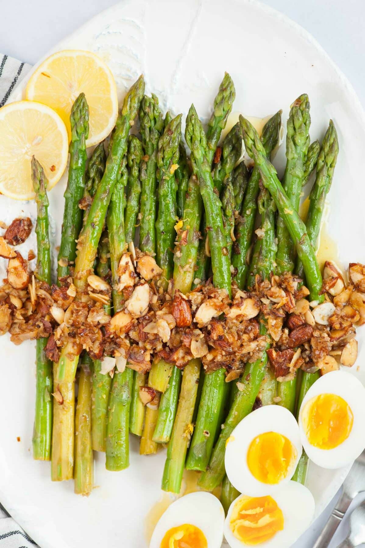 Asparagus almondine on a white plate with lemon slices and halved eggs on the side.