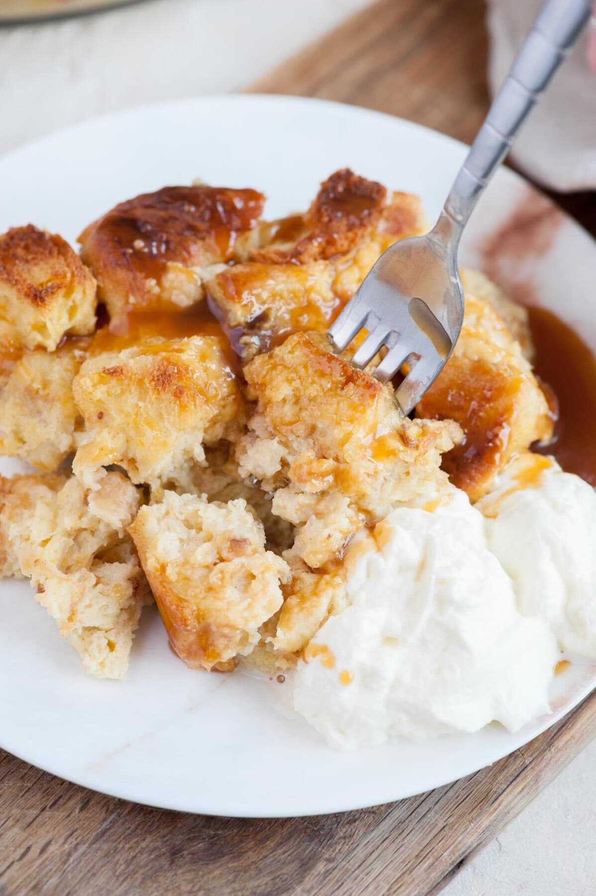 Brioche bread pudding served with caramel sauce and whipped cream on a white plate.