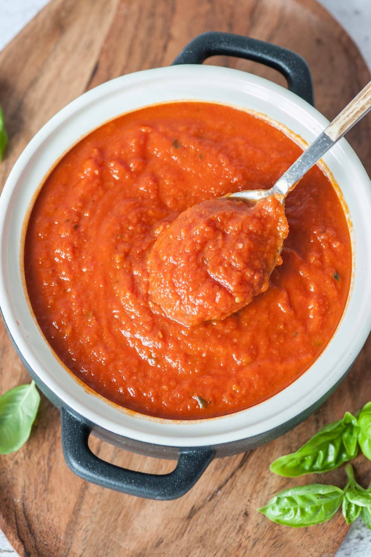 Marinara sauce in a white-black pot is being scooped with a spoon.