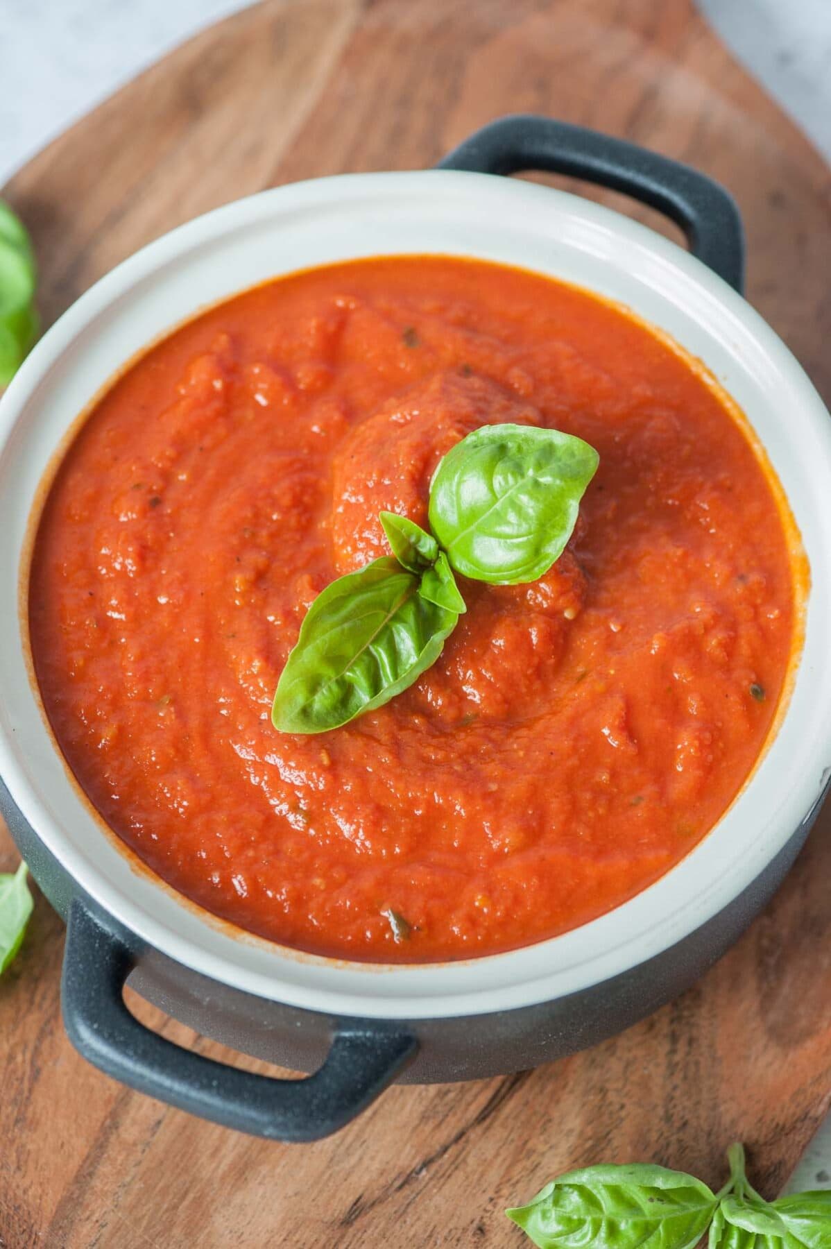 Marinara sauce in a white-black pot topped with basil leaves.