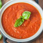 Marinara sauce in a white-black pot topped with basil leaves.