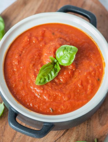 Marinara sauce in a white-black pot topped with basil leaves.