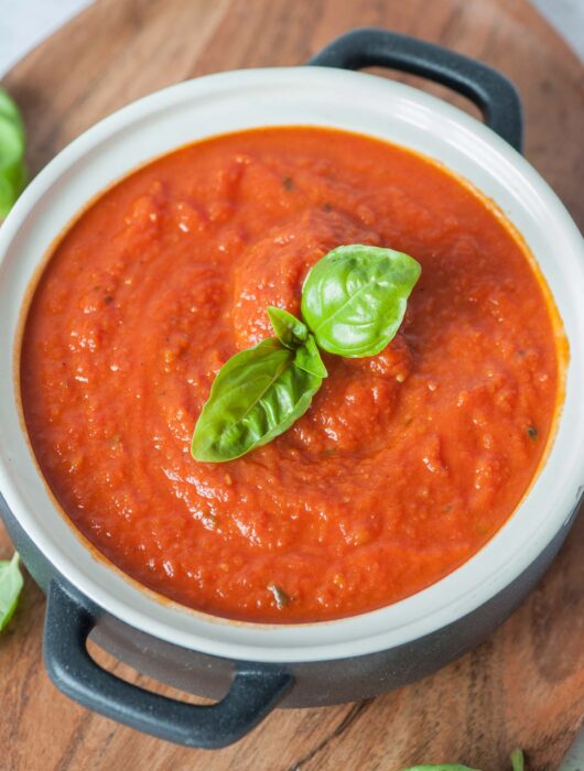 Marinara sauce in a white-black pot topped with basil leaves.
