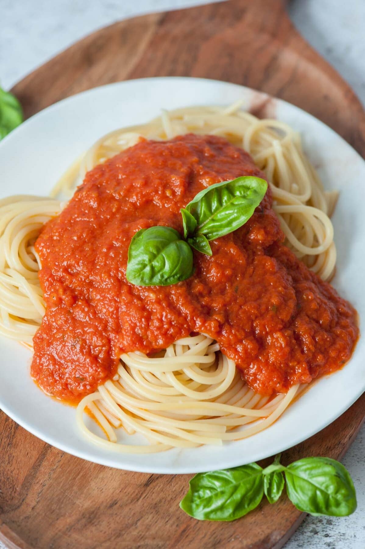 Makaron z sosem marinara na białym talerzu, udekorowany liśćmi bazylii.