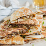 A stack of mushroom quesadillas on a beige wooden board.