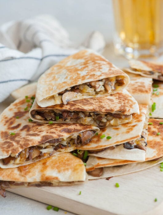 A stack of mushroom quesadillas on a beige wooden board.