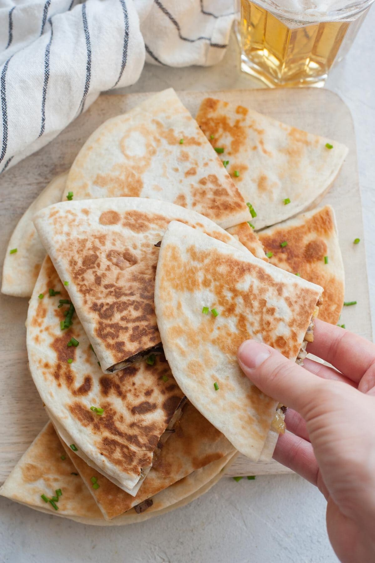 A hand is reaching for a quesadilla. Stack of quesadillas on a wooden board.