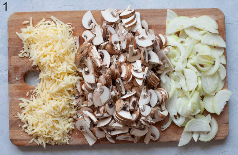 Chopped mushrooms, onions, and shredded cheese on a chopping board.