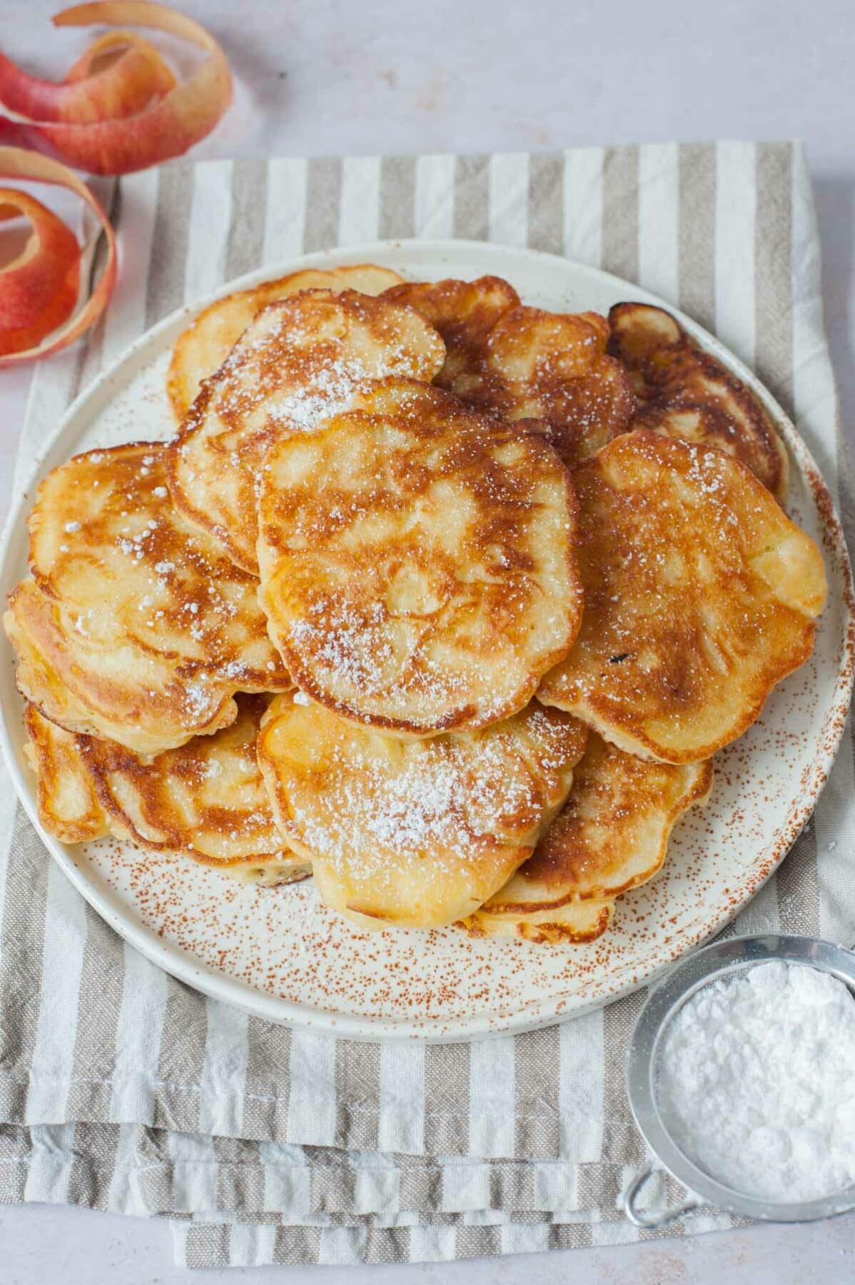 Polish apple pancakes dusted with powdered sugar on a white plate.