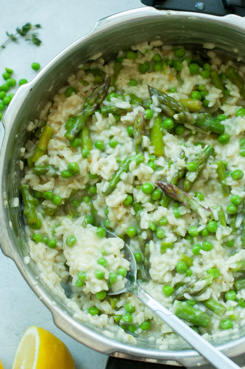 Asparagus risotto with peas in a pot with peas and lemons in the background.