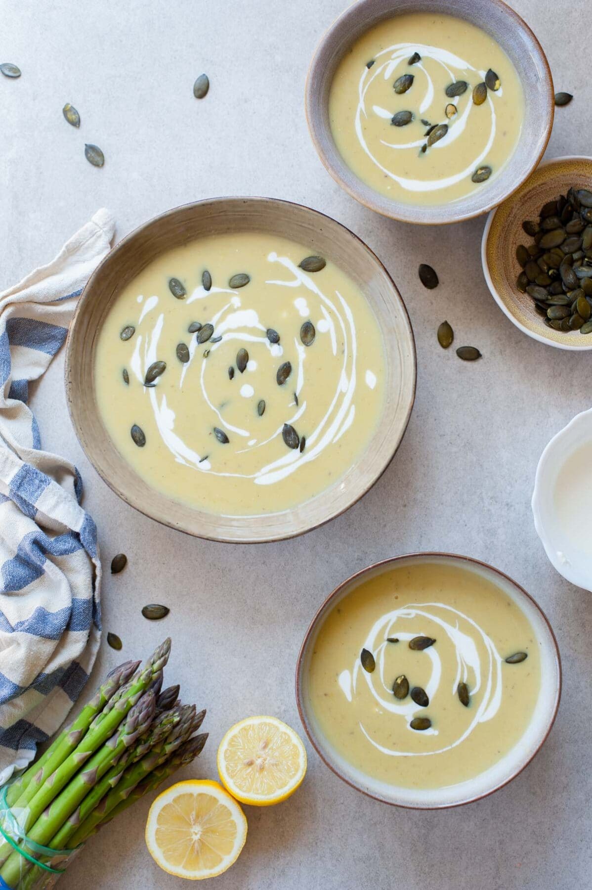 Three bowls with cream of asparagus soup topped with goat cheese and pepitas.