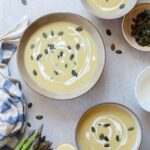 Three bowls with cream of asparagus soup topped with goat cheese and pepitas.