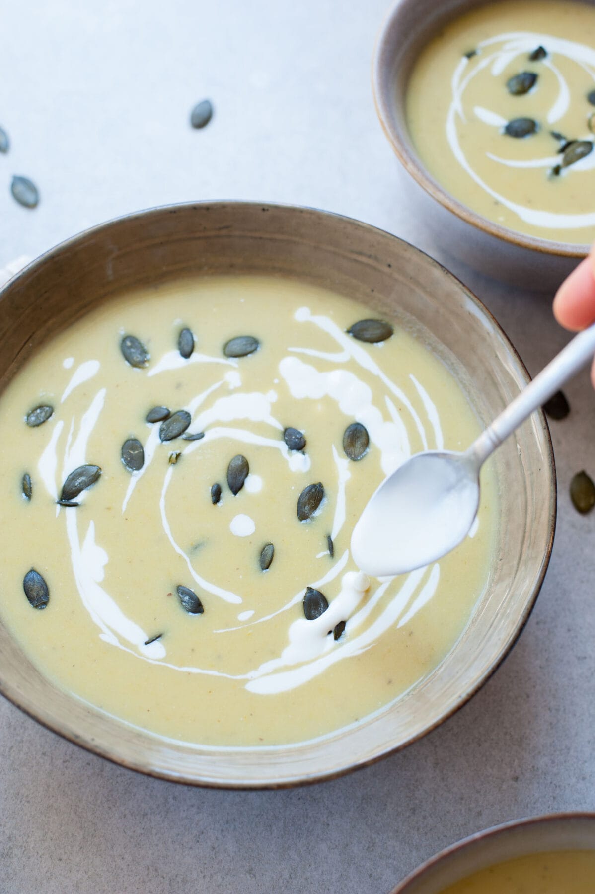 Goat cheese is being swirled into creamy asparagus soup in a green bowl.