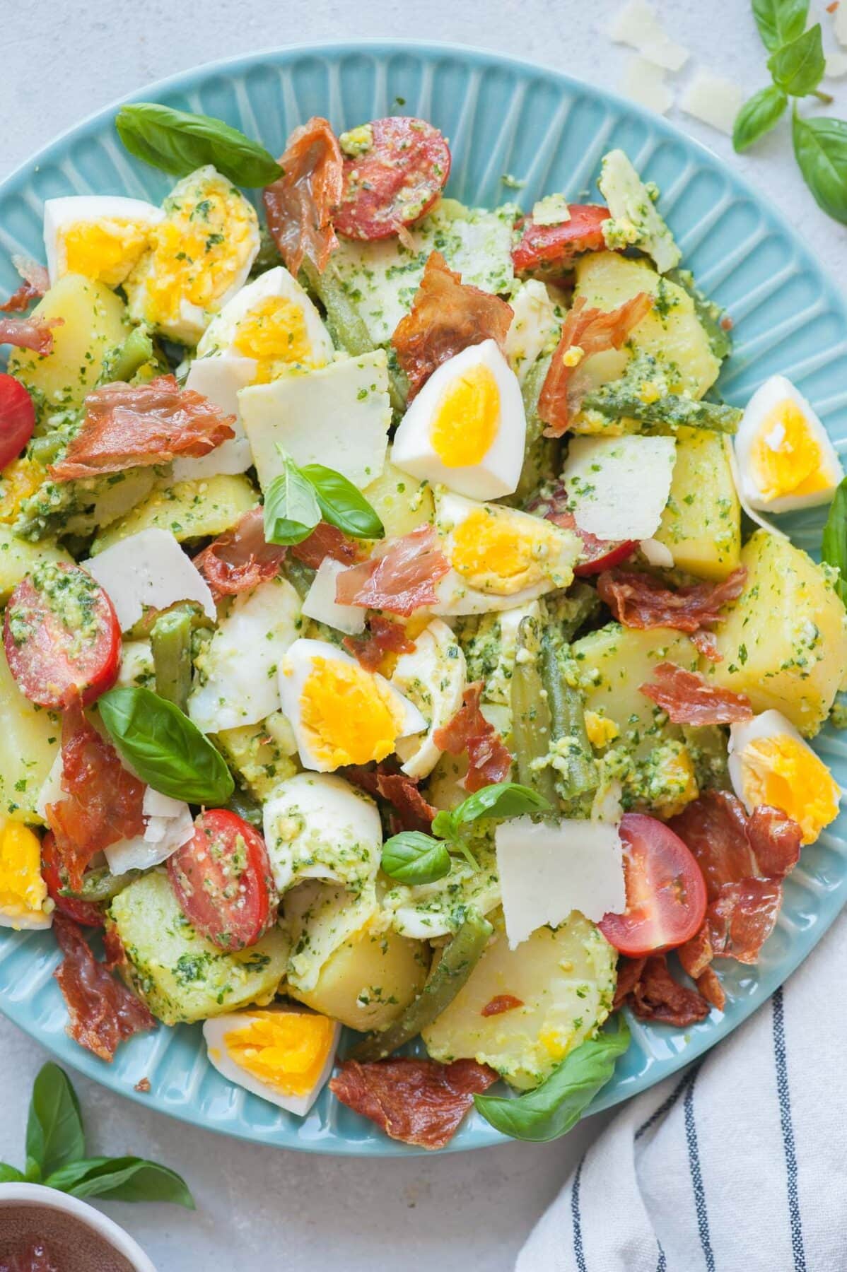 Pesto potato salad with eggs, green, beans, cherry tomatoes on a blue plate.