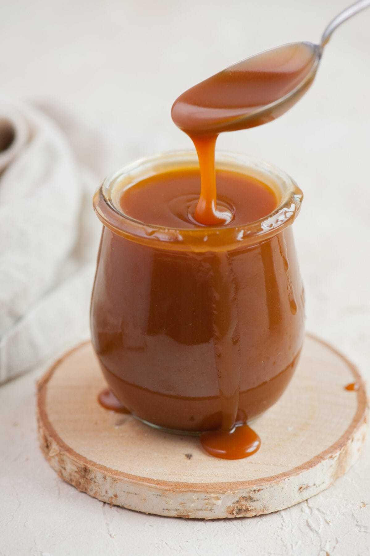 Salted caramel sauce is being poured from a teaspoon to a jar.