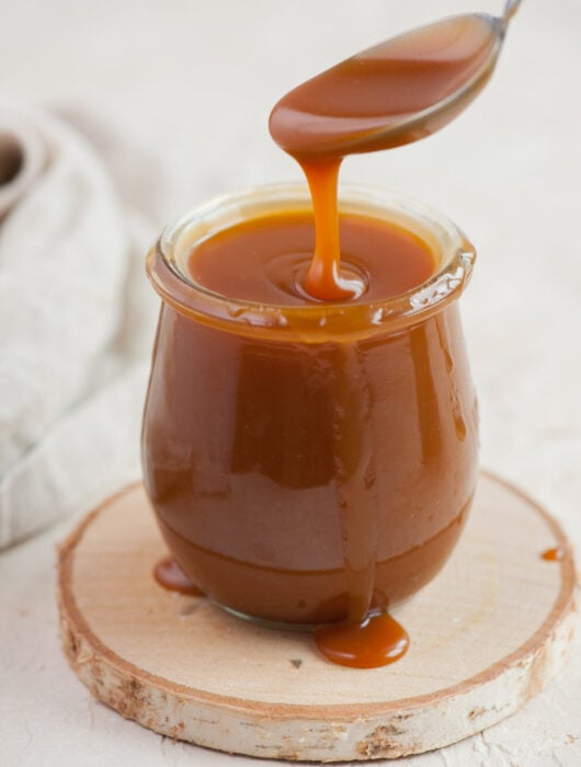 Salted caramel sauce in a jar is being spooned with a teaspoon.