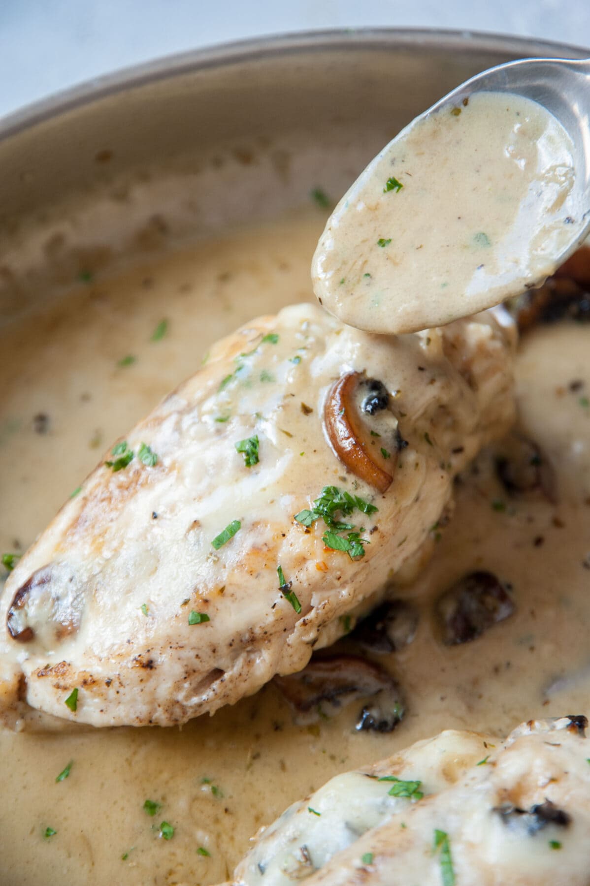 Mushroom stuffed chicken on a pan is being poured with a creamy sauce.