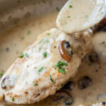 Mushroom stuffed chicken on a pan is being poured with a creamy sauce.