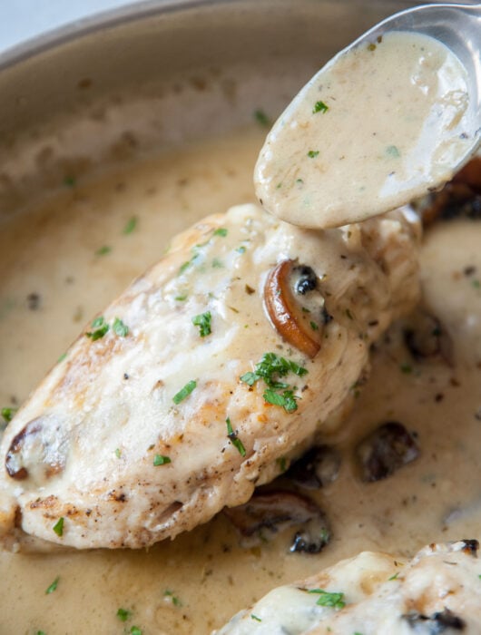Mushroom stuffed chicken on a pan is being poured with a creamy sauce.