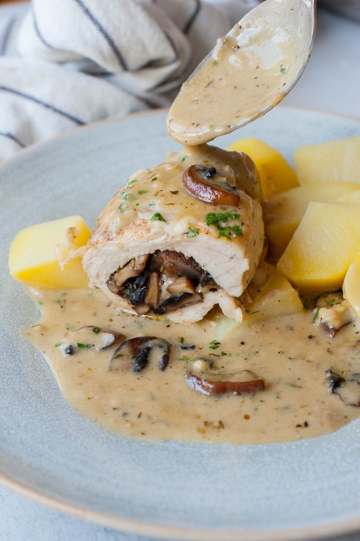 Mushroom stuffed chicken breast cut in half is being poured with creamy sauce.