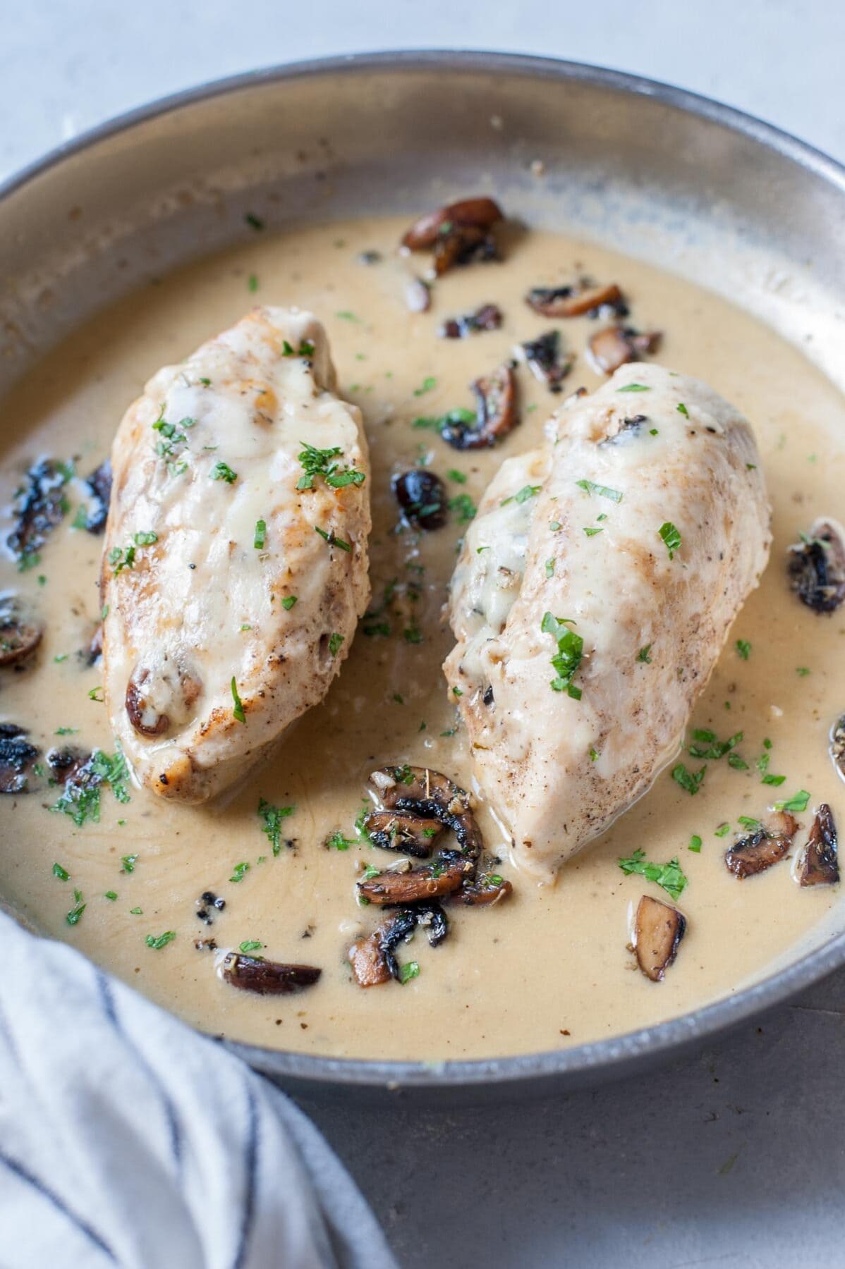 Two chicken breasts stuffed with mushrooms and cheese on a pan with creamy sauce sprinkled with parsley.
