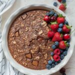 Baked chocolate oatmeal in a white baking dish topped with fresh berries.