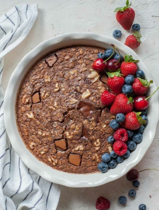 Baked chocolate oatmeal in a white baking dish topped with fresh berries.