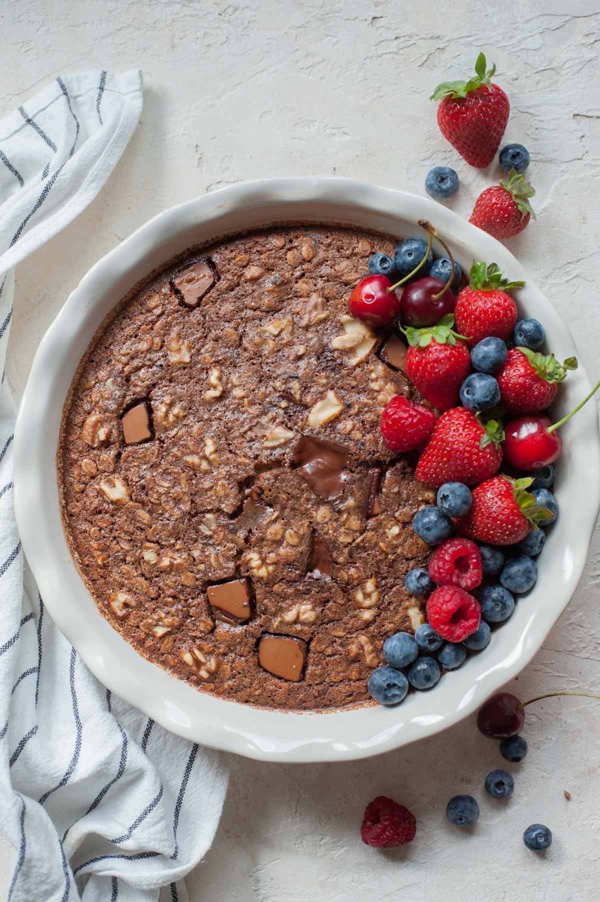 Chocolate oatmeal in a white baking dish topped with fresh berries.
