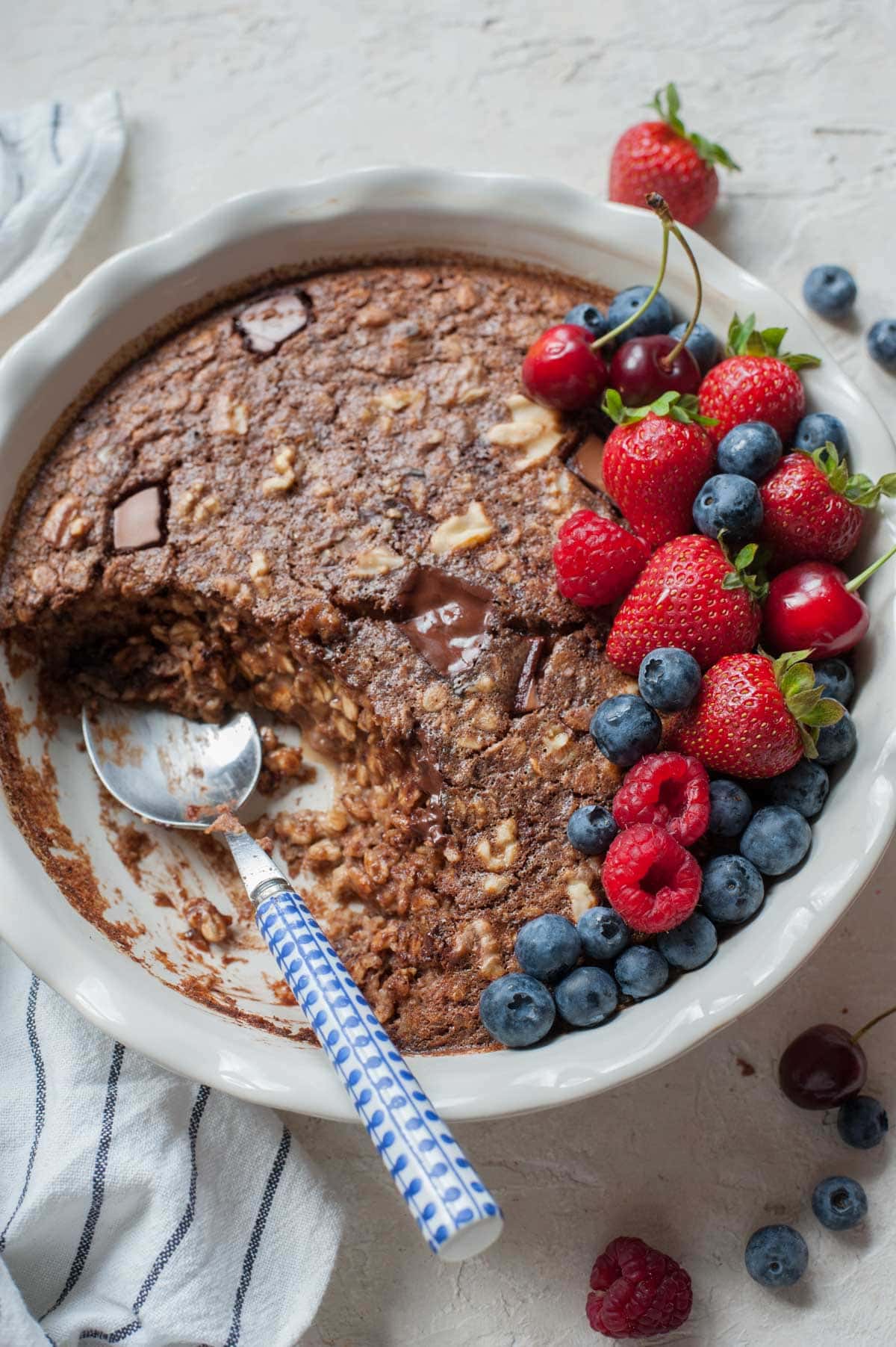 Chocolate oatmeal in a white baking dish with a piece missing topped with fresh berries.