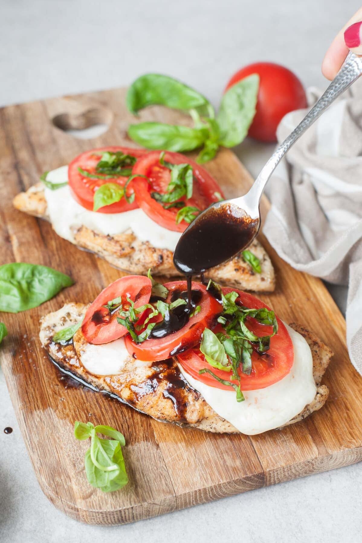 Caprese chicken on a wooden board is being drizzled with balsamic glaze.