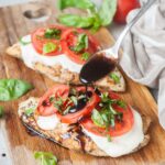 Caprese chicken on a wooden board is being drizzled with balsamic glaze.