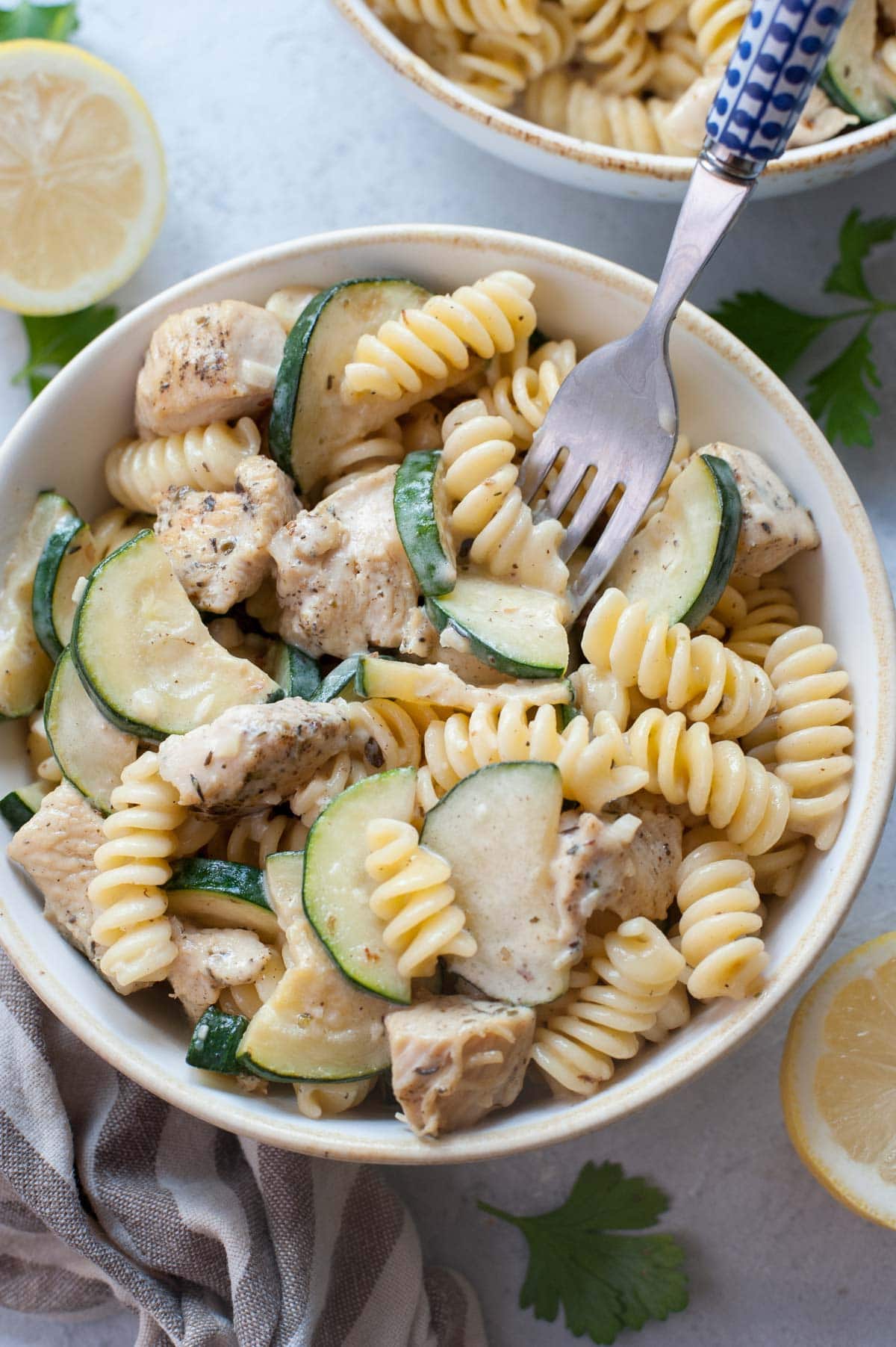 Chicken zucchini pasta in a white bowl is being picked with a fork.