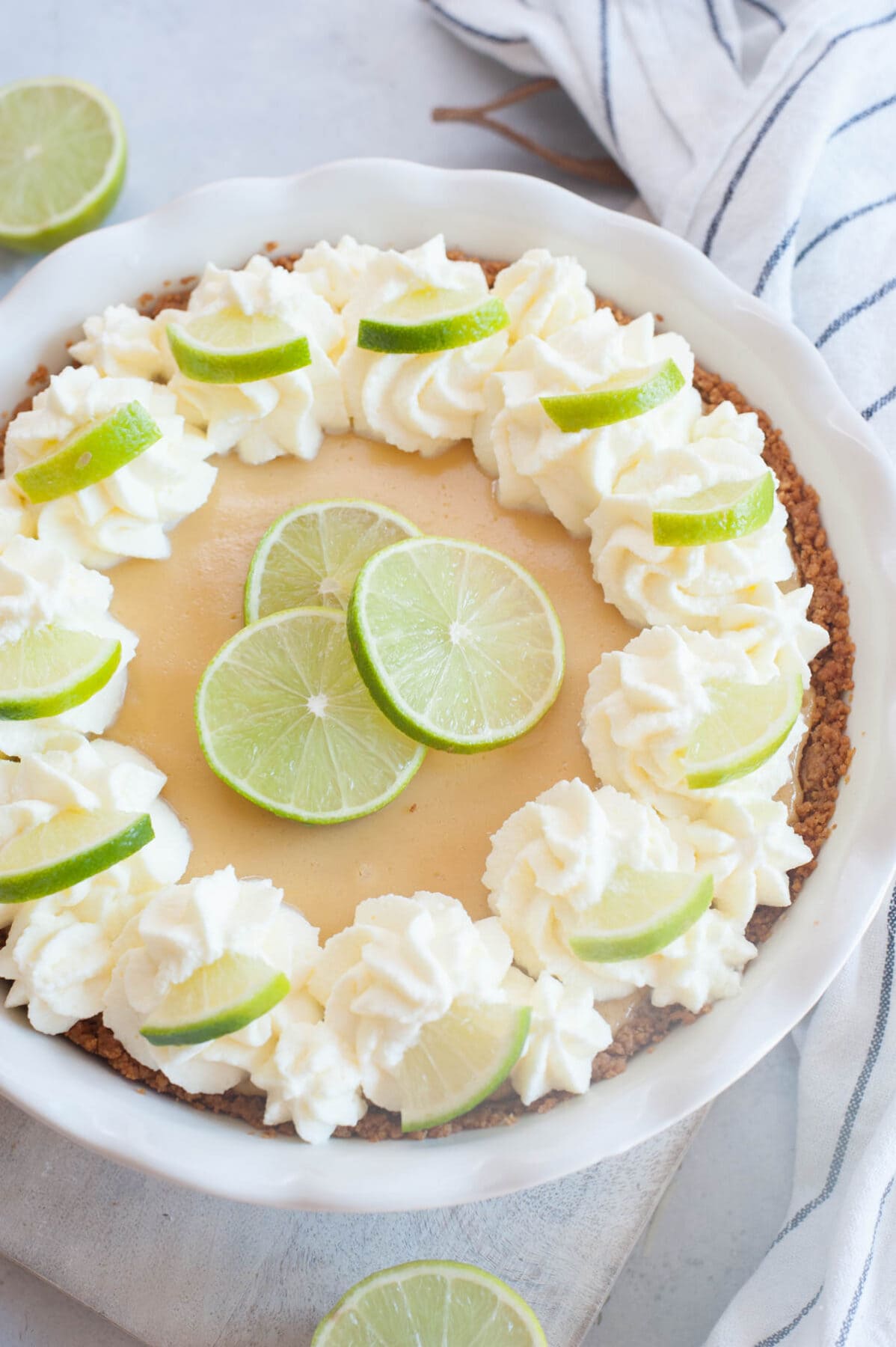 Key lime pie in a pie dish topped with whipped cream and lime slices.