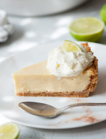 A slice of key lime pie on a white plate topped with whipped cream.