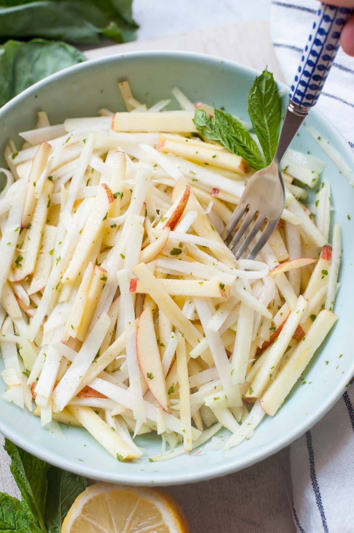 Kohlrabi apple slaw in a green bowl is being picked with a fork.