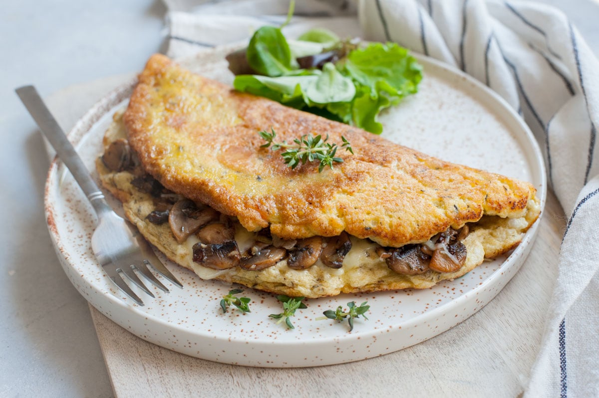 Fluffy omelet filled with mushrooms and cheese on a white plate.