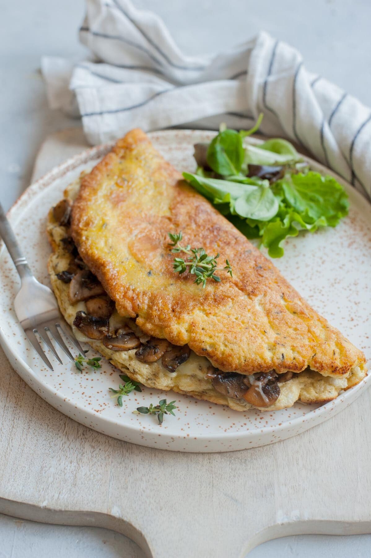 Fluffy omelet filled with mushrooms and cheese on a white plate.